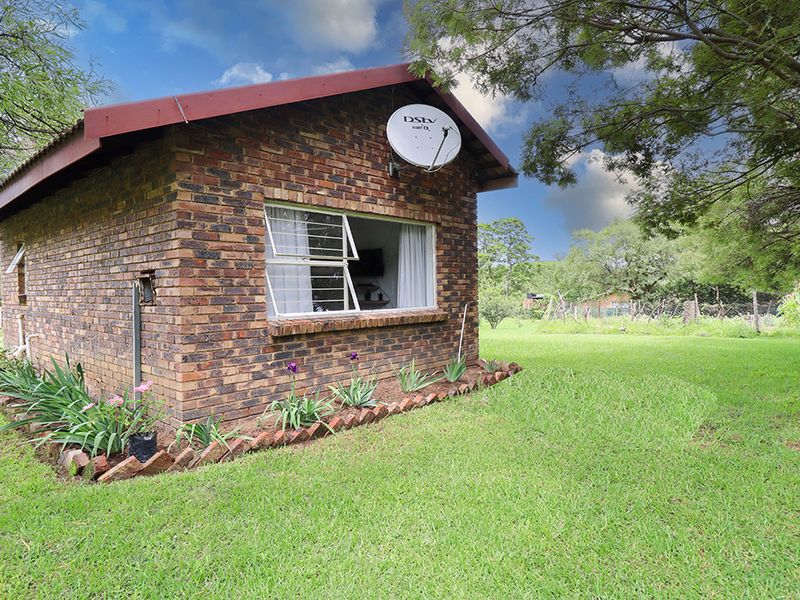 A view of the rear exterior of the cottage featuring face brick construction, a corrugated metal roof, and established garden surroundings.