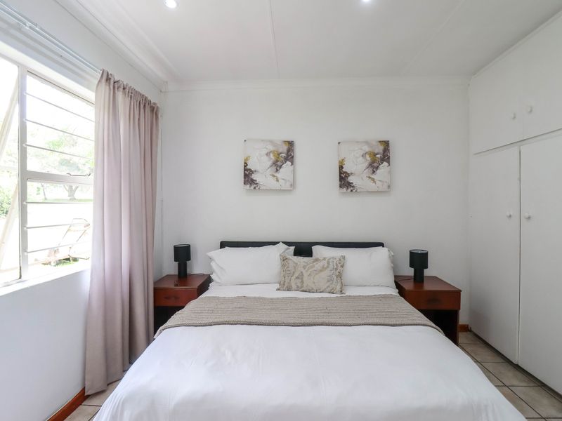 A bright and tidy bedroom featuring built-in cupboards, tiled flooring, and a large window allowing for natural light.