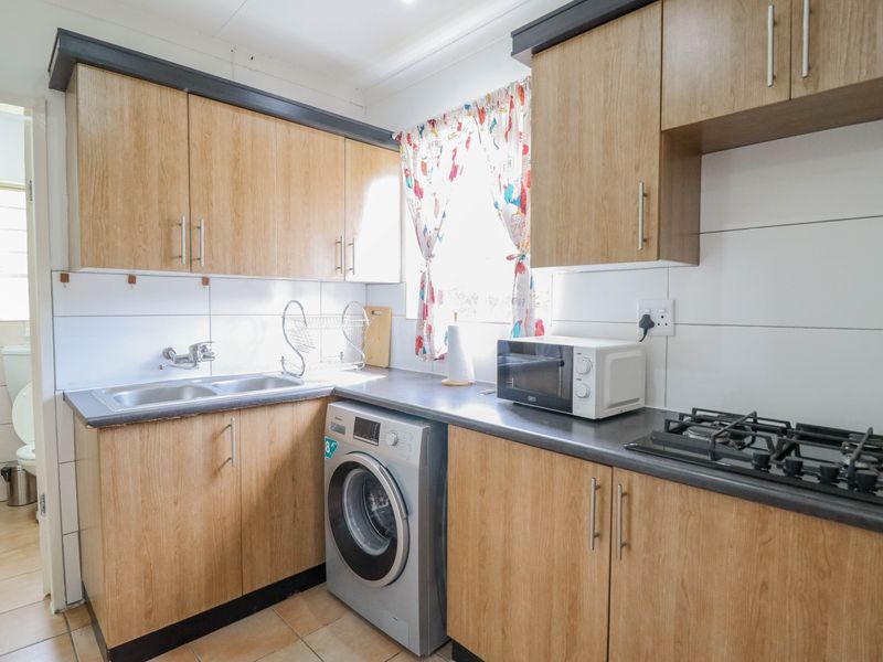 Compact kitchen featuring wood-look laminate cabinetry, a gas hob, double bowl sink, and tiled splashback with direct access to an adjacent bathroom area.