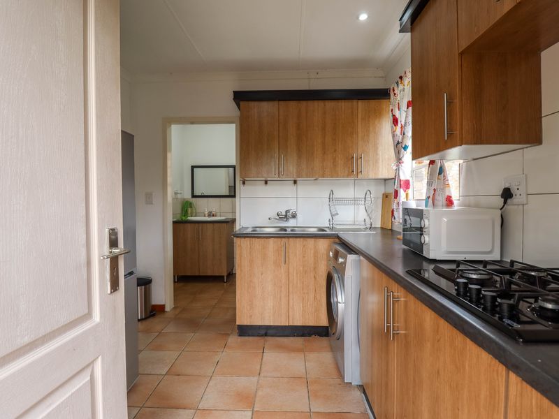 Functional kitchen featuring wood-look cabinetry, dark countertops, gas hob, and tiled flooring, with an adjacent scullery area visible through the doorway.