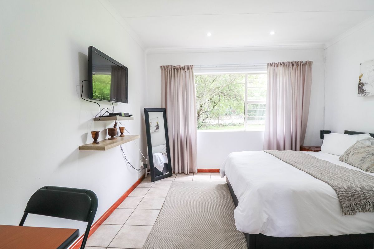 A bright bedroom featuring tiled flooring, recessed downlighting, and a window with security bars, offering a clean and functional living space.