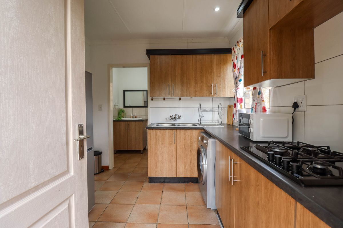 Functional kitchen featuring wood-look cabinetry, dark countertops, gas hob, and tiled flooring, with an adjacent scullery area visible through the doorway.