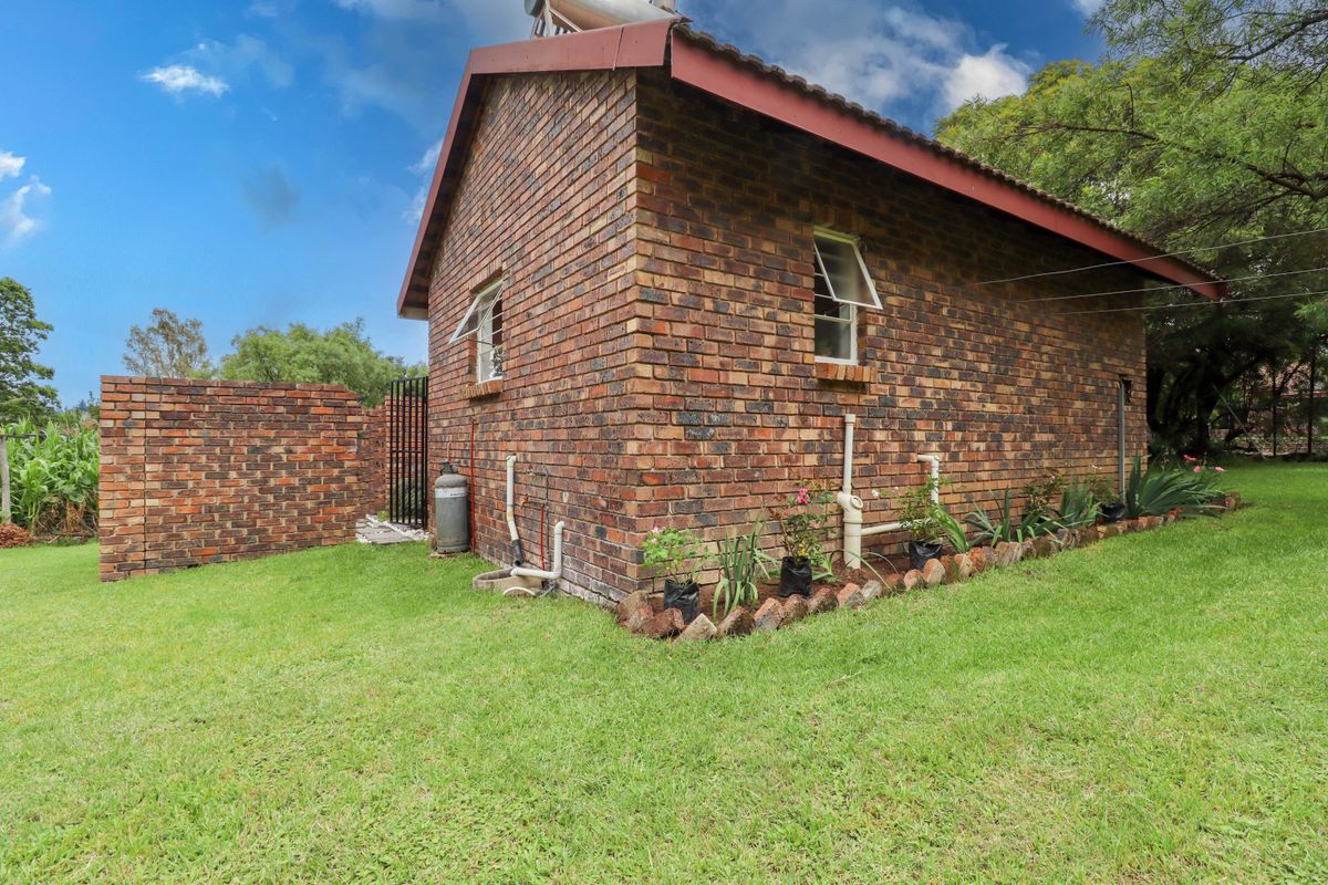 Rear view of a face brick cottage featuring a tiled roof, solar water heater, and surrounding garden space with a brick boundary wall.