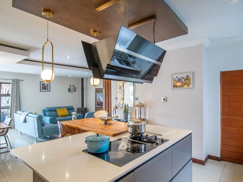 Modern open-plan living area featuring a central kitchen island with a built-in hob, extractor fan, and stone countertops, flowing into the dining and lounge space.