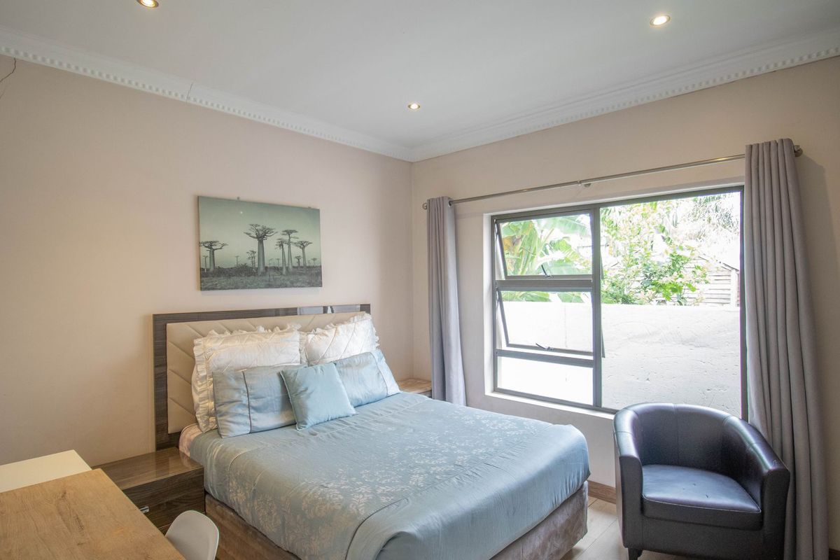A bedroom featuring recessed downlights, decorative cornice, and built-in cupboards, with a window overlooking the exterior area.