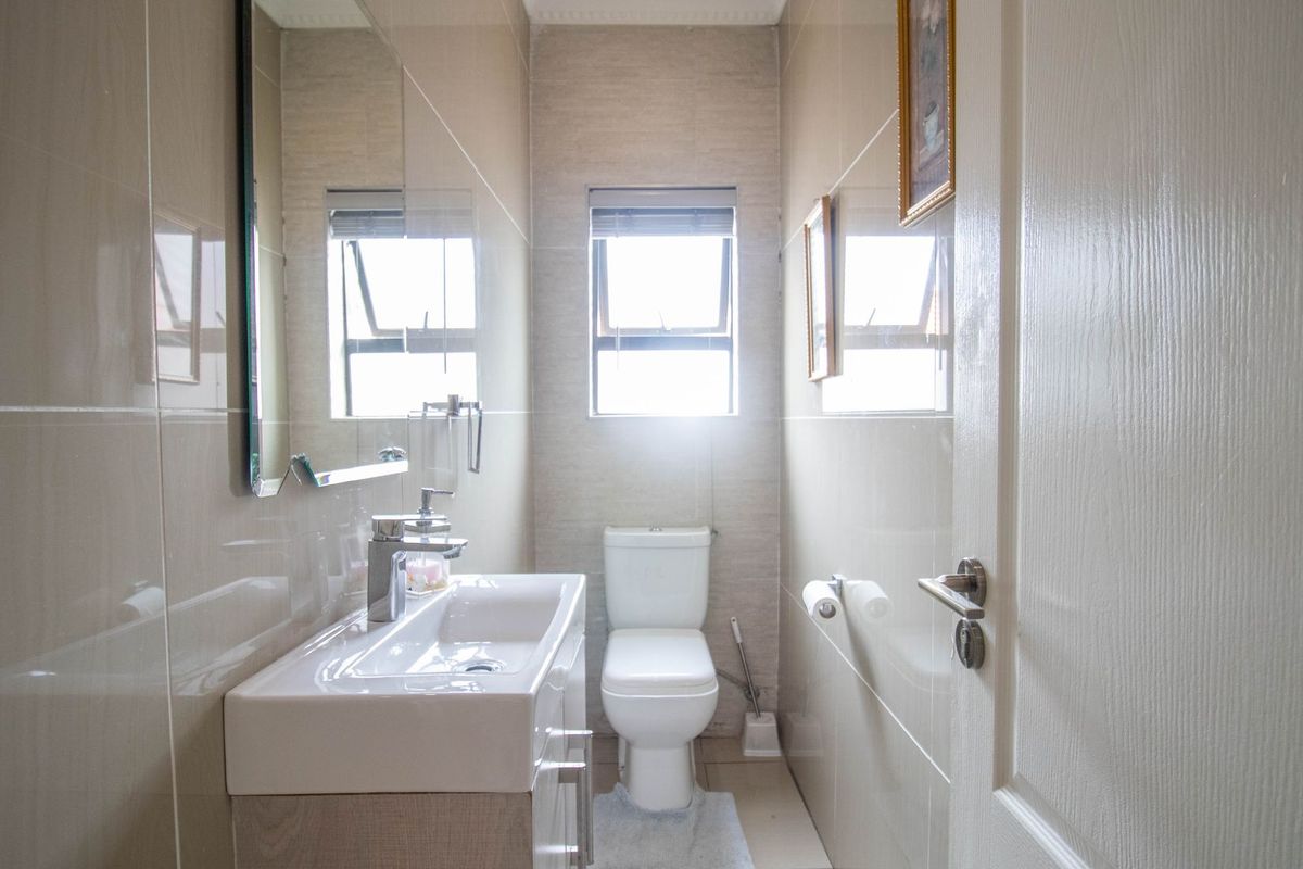 A clean, modern bathroom featuring a vanity cabinet with a ceramic basin, chrome mixer tap, wall-mounted mirror, and a toilet with tiled finishes.