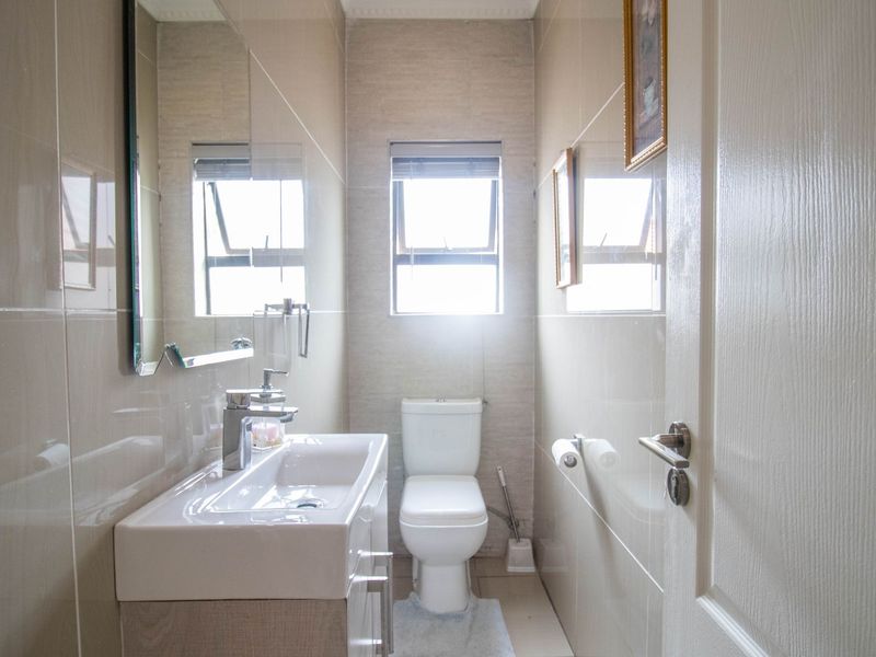 A clean, modern bathroom featuring a vanity cabinet with a ceramic basin, chrome mixer tap, wall-mounted mirror, and a toilet with tiled finishes.