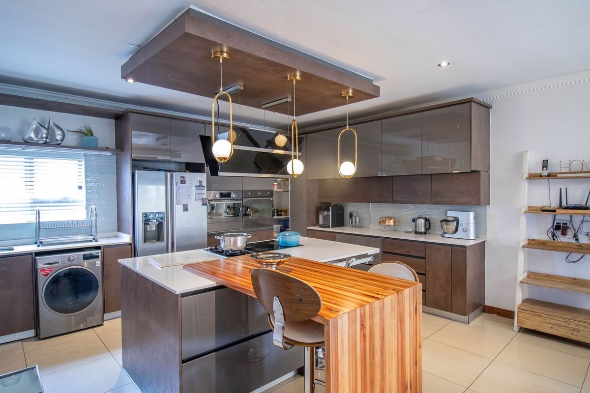 Modern kitchen featuring a central island with a wooden breakfast bar, high-gloss cabinetry, built-in appliances, and contemporary pendant lighting.