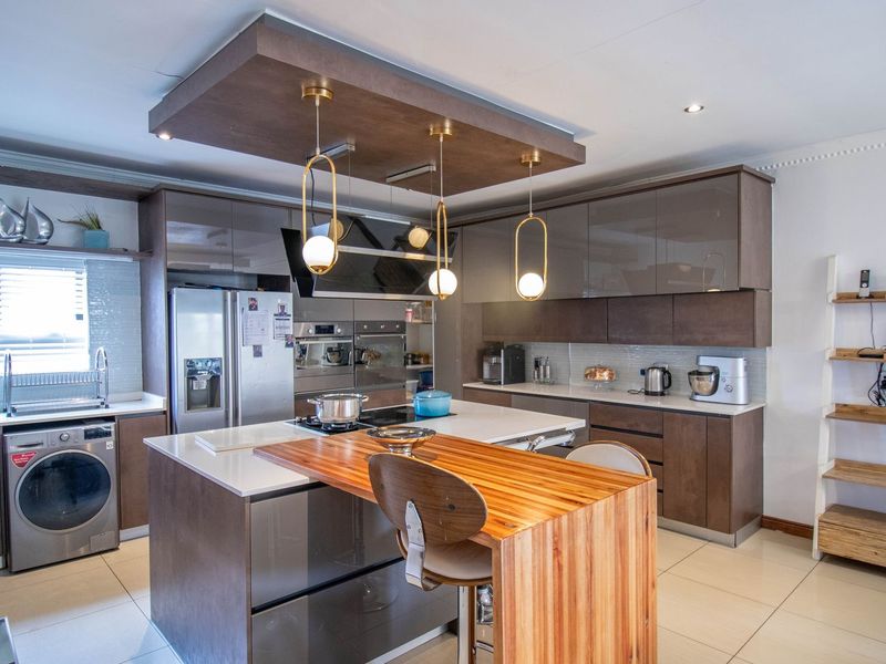 Modern kitchen featuring a central island with a wooden breakfast bar, high-gloss cabinetry, built-in appliances, and contemporary pendant lighting.