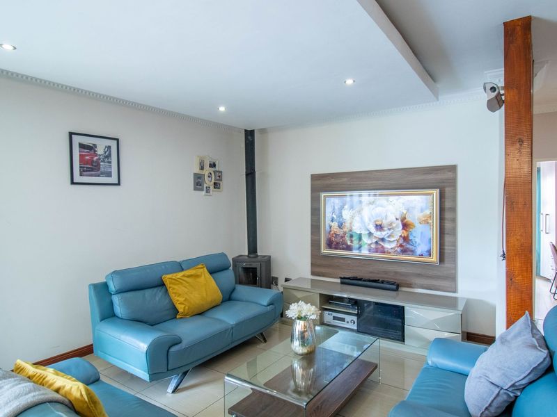 A well-maintained living room featuring a wood-burning fireplace, recessed ceiling with downlights, and a built-in media unit with tiled flooring.