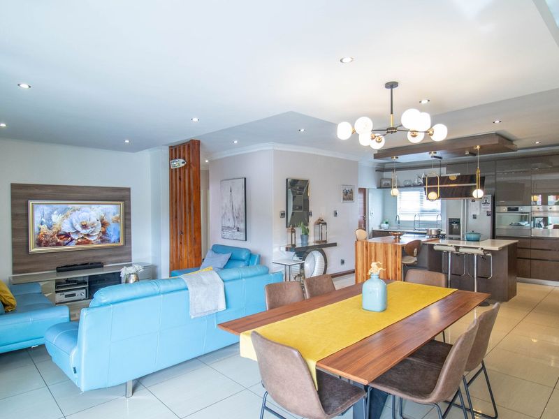 Spacious open-plan living, dining, and kitchen area featuring modern cabinetry, a central island, tiled flooring, and a built-in wood-burning fireplace.