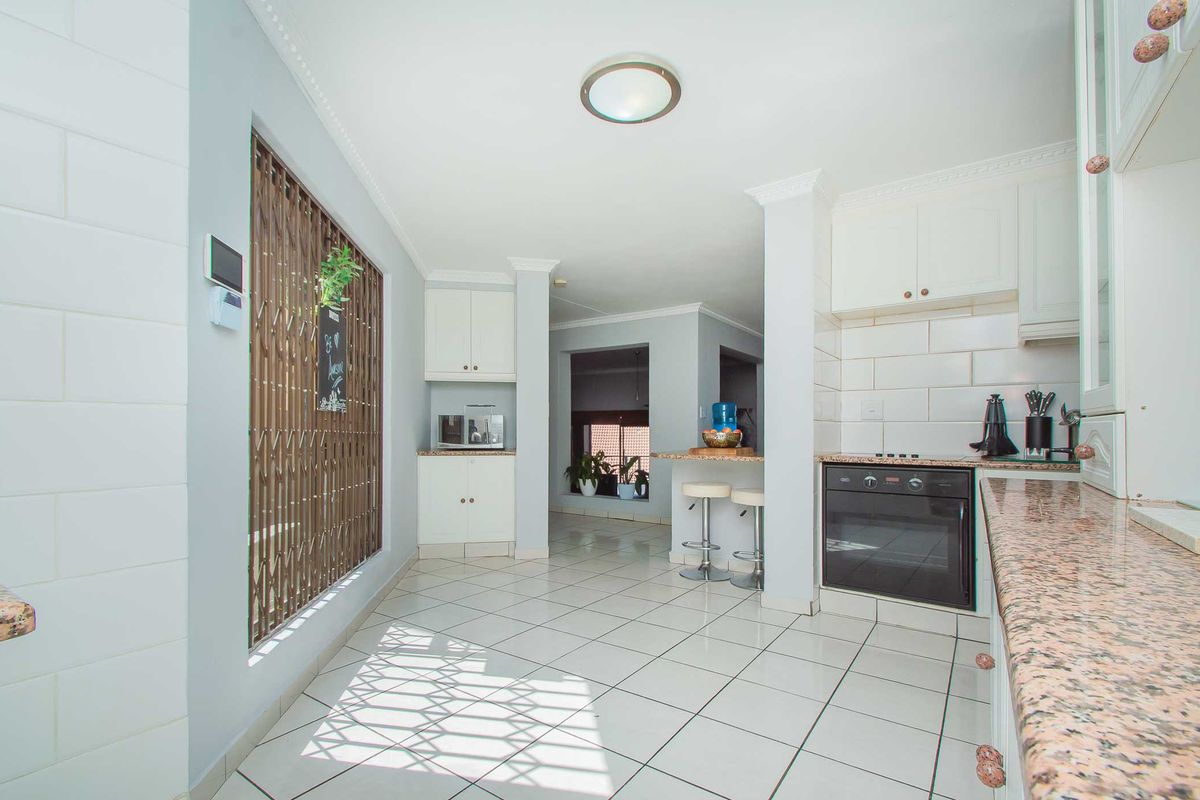 A functional kitchen featuring granite countertops, built-in oven, hob, and white cabinetry, with tiled flooring and a breakfast bar area.