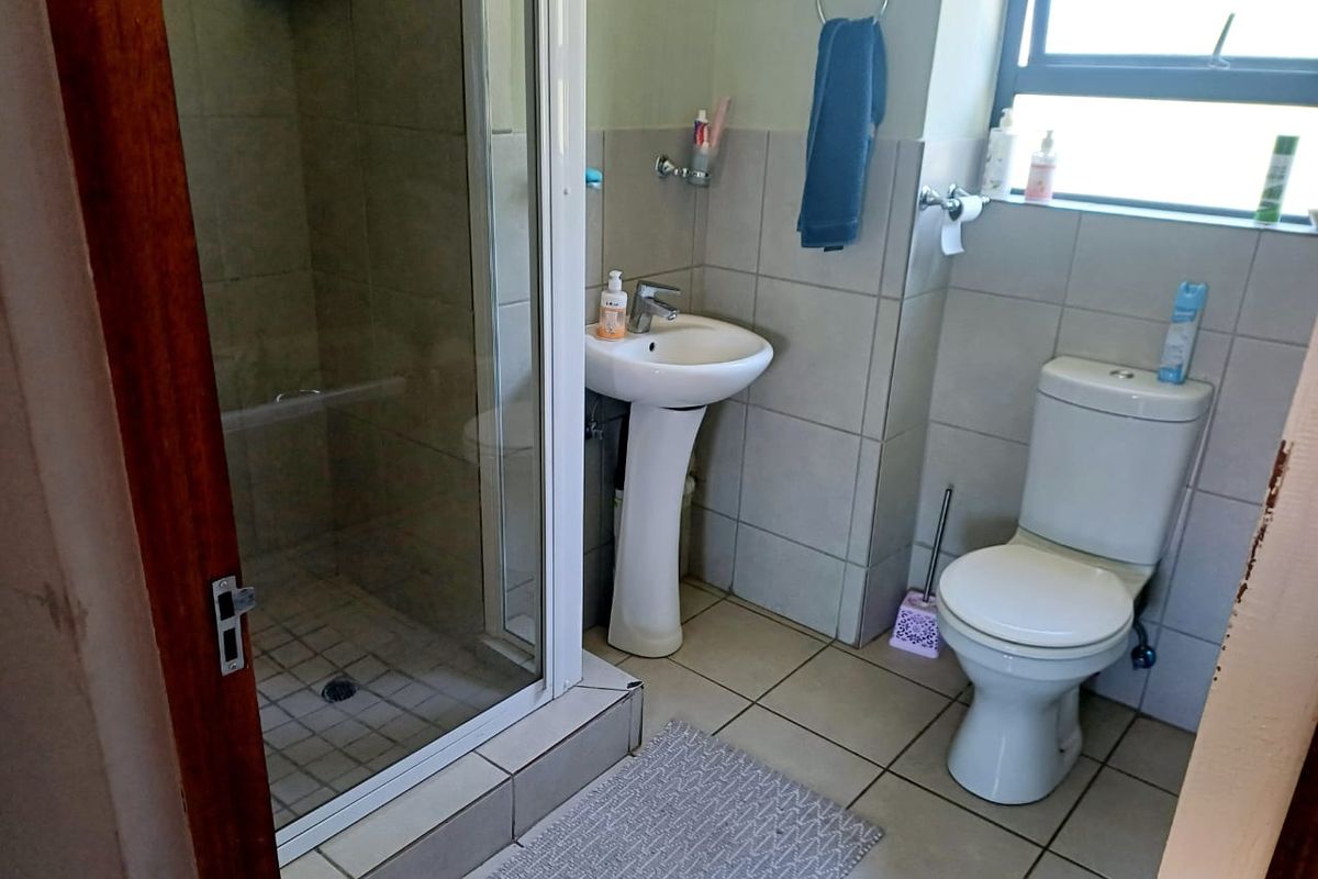 A functional bathroom featuring a glass-enclosed shower, pedestal basin, and standard toilet with neutral wall and floor tiling.