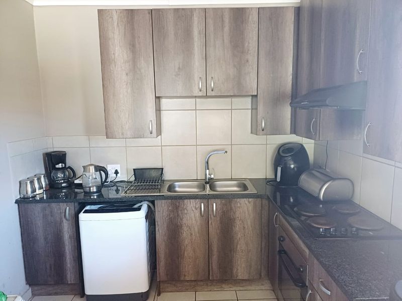A functional kitchen featuring wood-look laminate cabinetry, granite countertops, a double bowl sink, and integrated electric cooking appliances with a tiled backsplash.