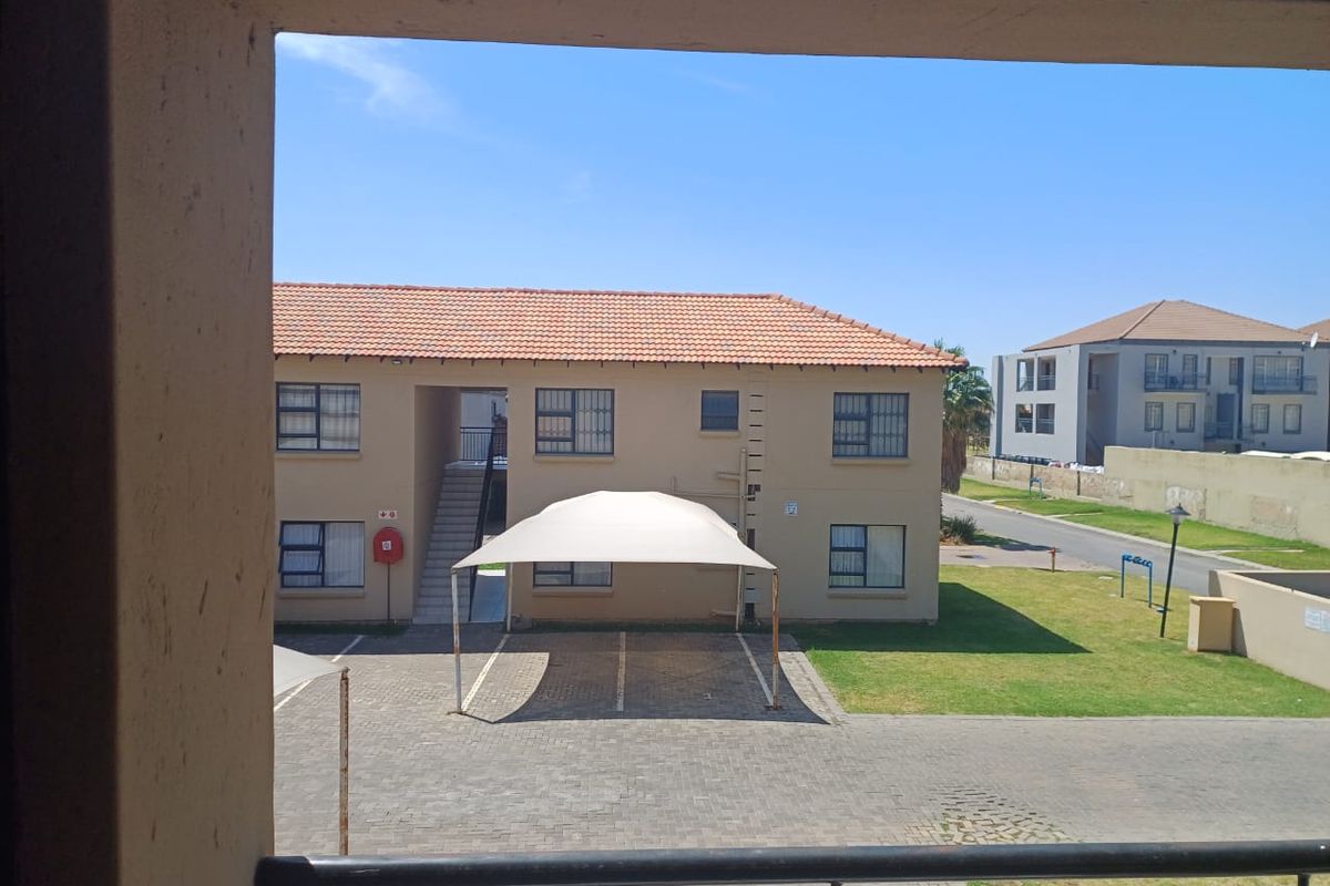 View from an elevated position overlooking the apartment complex grounds, featuring a paved parking area with a shade cloth carport and surrounding lawn.