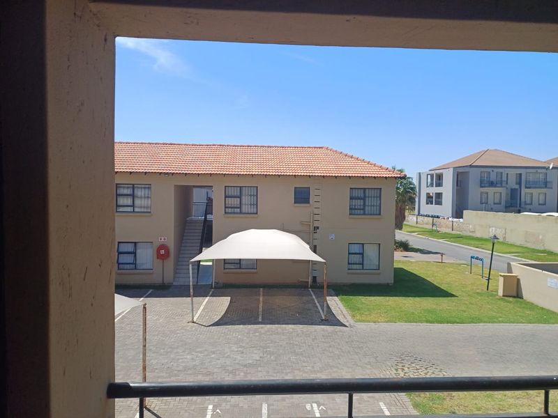 View from an elevated position overlooking the apartment complex grounds, featuring a paved parking area with a shade cloth carport and surrounding lawn.
