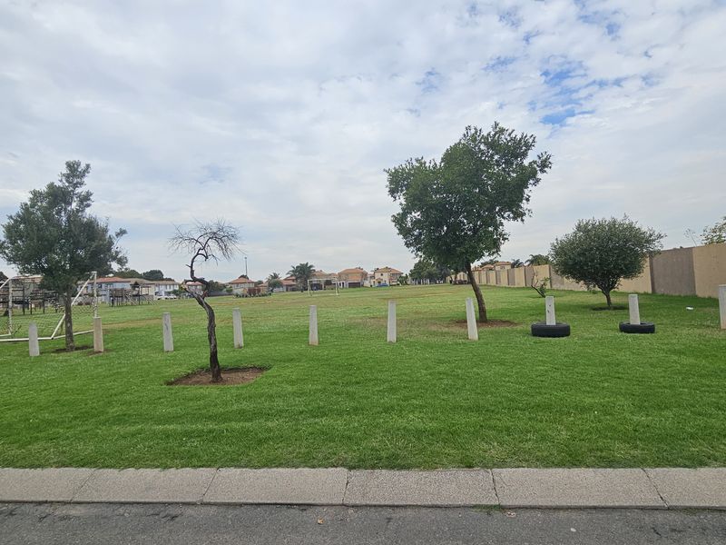 A well-maintained communal green space featuring manicured lawn, mature trees, and concrete perimeter security bollards.