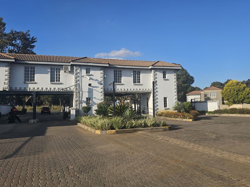 The front entrance of the apartment complex features a secure gatehouse, paved driveway, and well-maintained landscaped garden beds.