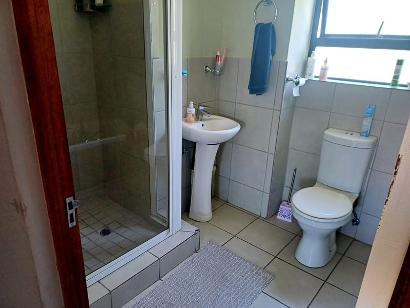 A functional bathroom featuring a pedestal basin, a glass-enclosed shower, and a standard toilet with neutral wall and floor tiling.