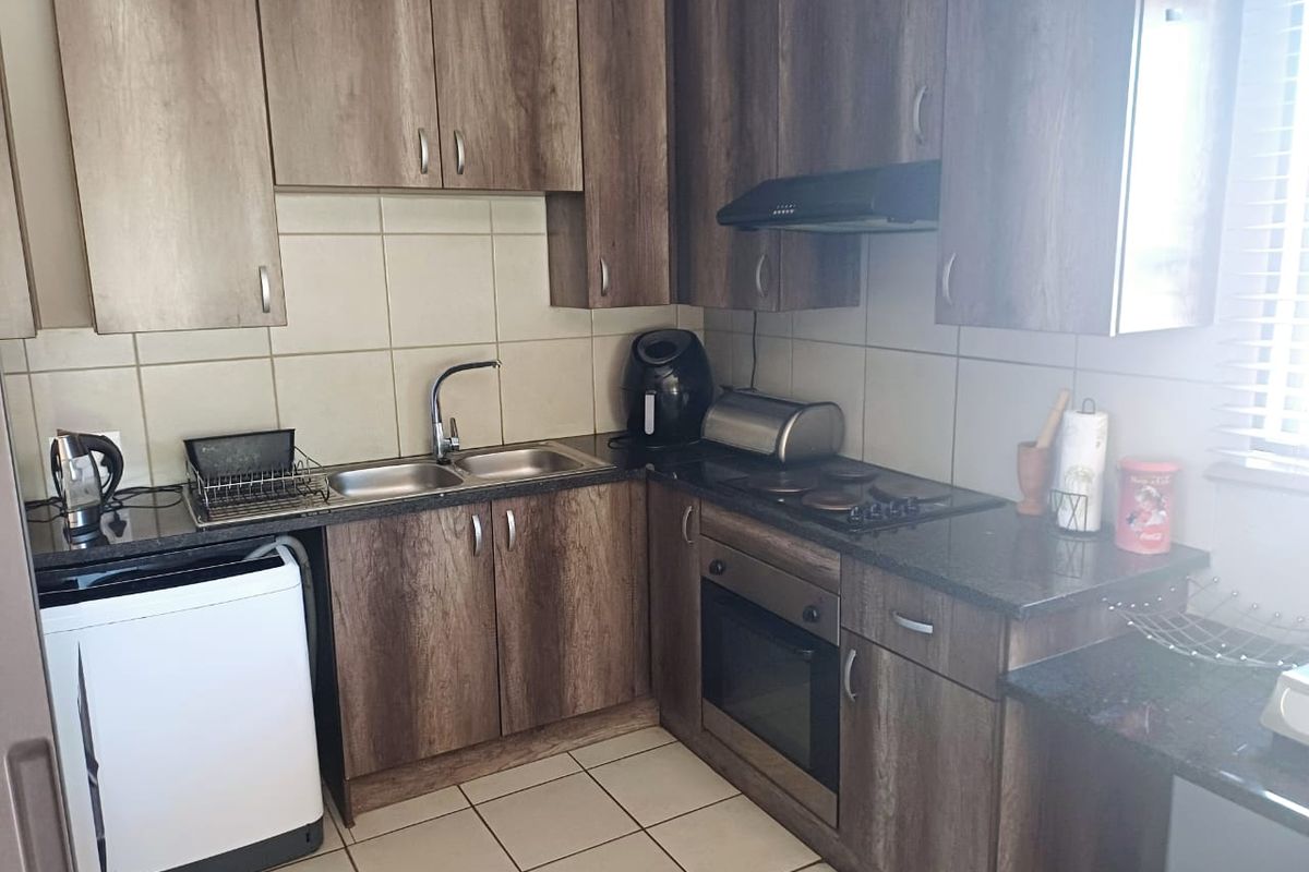 A functional kitchen featuring wood-look laminate cabinetry, granite countertops, a built-in oven with hob, and a tiled backsplash.