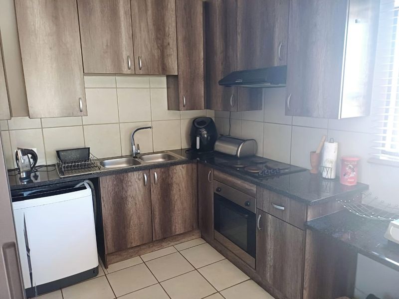 A functional kitchen featuring wood-look laminate cabinetry, granite countertops, a built-in oven with hob, and a tiled backsplash.