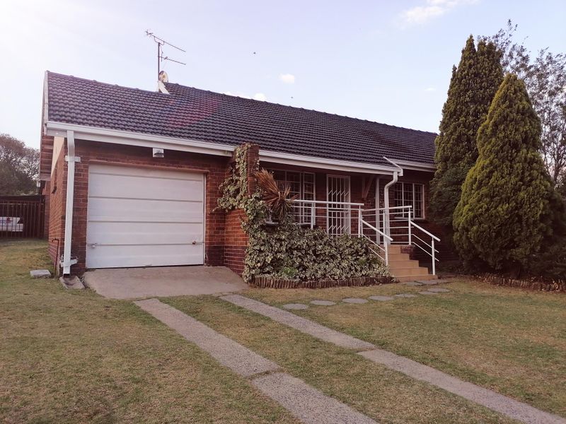 Front elevation of a single-story brick house featuring a single garage, concrete driveway, and elevated entrance with security railing.