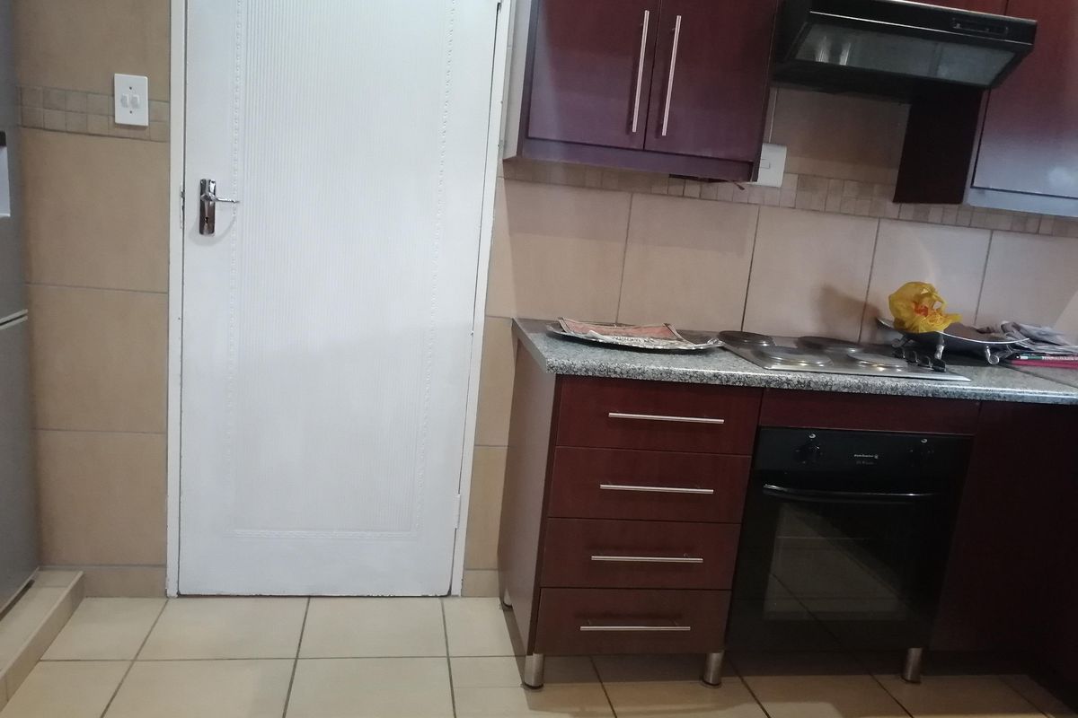 A functional kitchen featuring dark wood cabinetry, granite countertops, built-in oven, electric hob, and tiled finishes throughout.