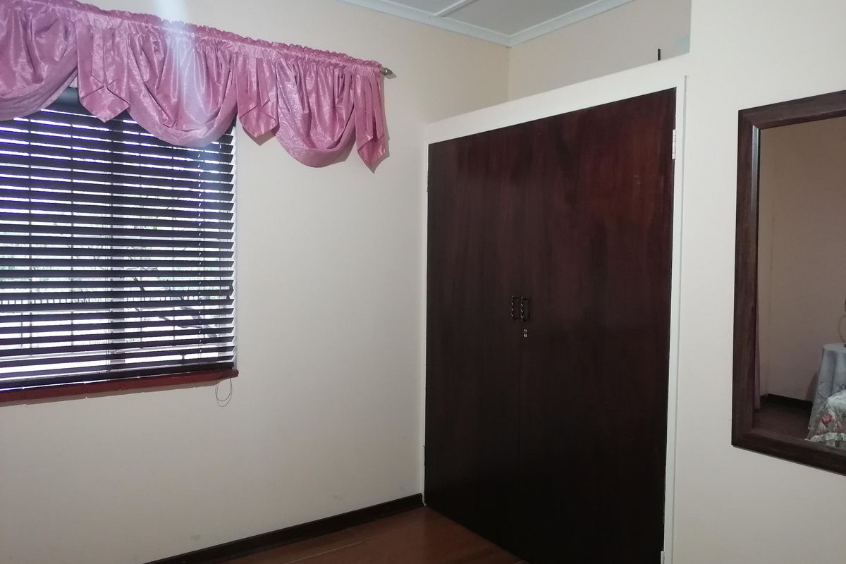 A clean bedroom featuring laminate flooring, a built-in wardrobe, and venetian blinds, offering a neutral space ready for personalization.