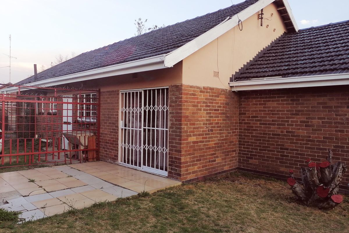 Rear view of the property featuring a brick facade, tiled roof, and a paved patio area secured with metal gates.