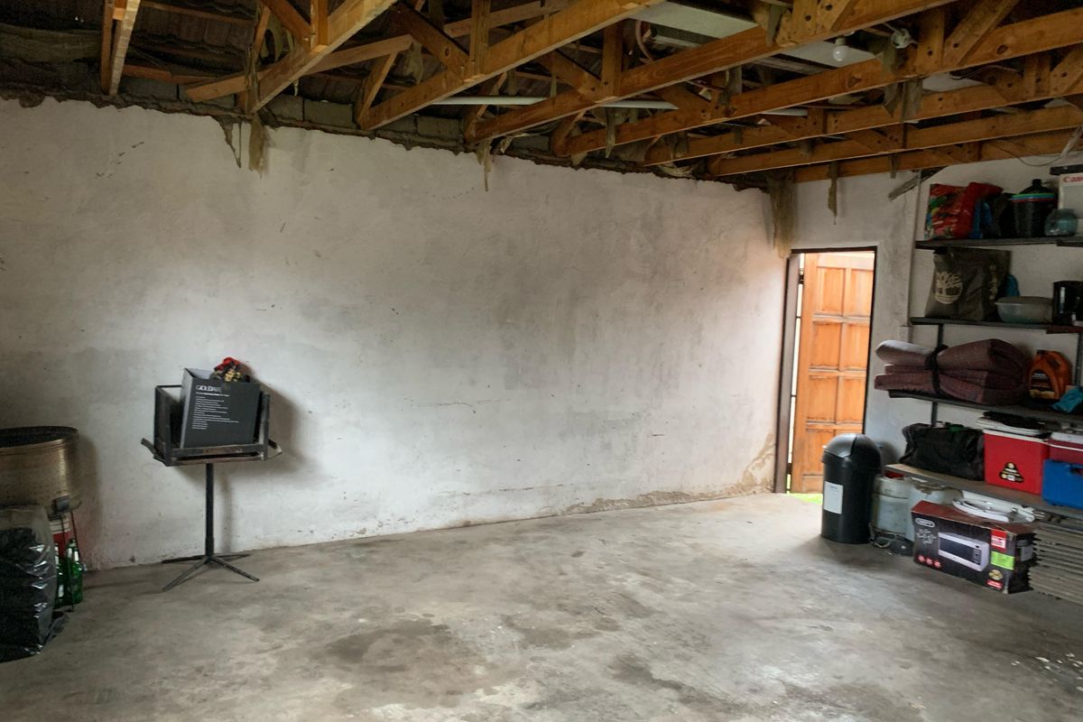 An unfinished garage space featuring exposed timber roof trusses, concrete flooring, and plastered masonry walls, offering potential for renovation or storage conversion.