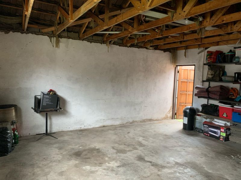 An unfinished garage space featuring exposed timber roof trusses, concrete flooring, and plastered masonry walls, offering potential for renovation or storage conversion.