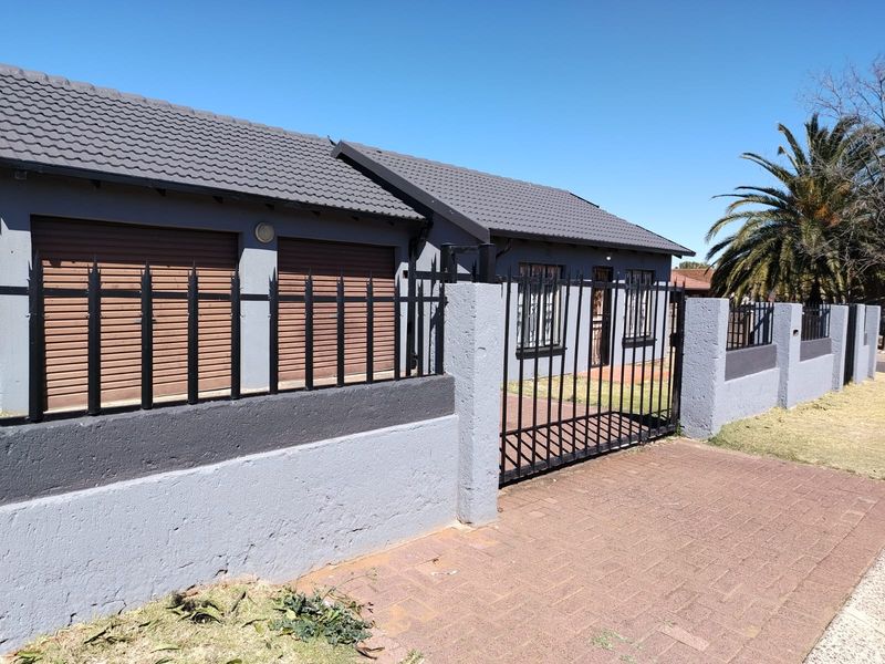 Front exterior view of a house featuring a tiled roof, roller shutter garage doors, and a secure perimeter wall with metal fencing.