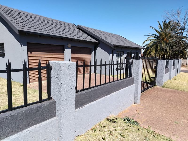 Front view of a modern house featuring a double garage, paved driveway, and secure perimeter wall with metal fencing.