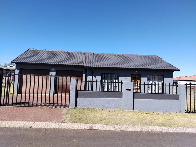 Front elevation of a modern single-story house featuring a tiled roof, double garage with roller doors, and secure perimeter wall with metal fencing.