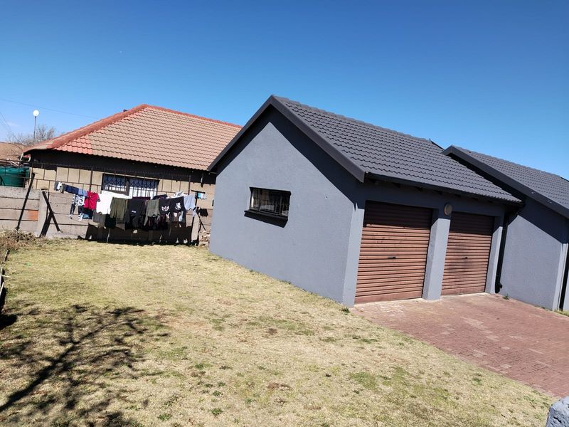 Rear view of the property featuring a double garage with roller doors, paved driveway, and a surrounding boundary wall.