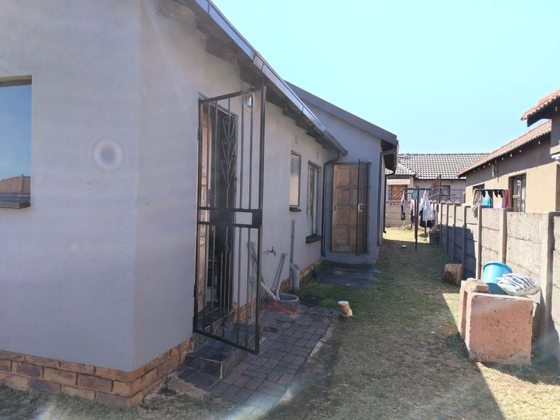 Rear exterior view of the property featuring a paved walkway, security gates, and a precast concrete boundary wall.