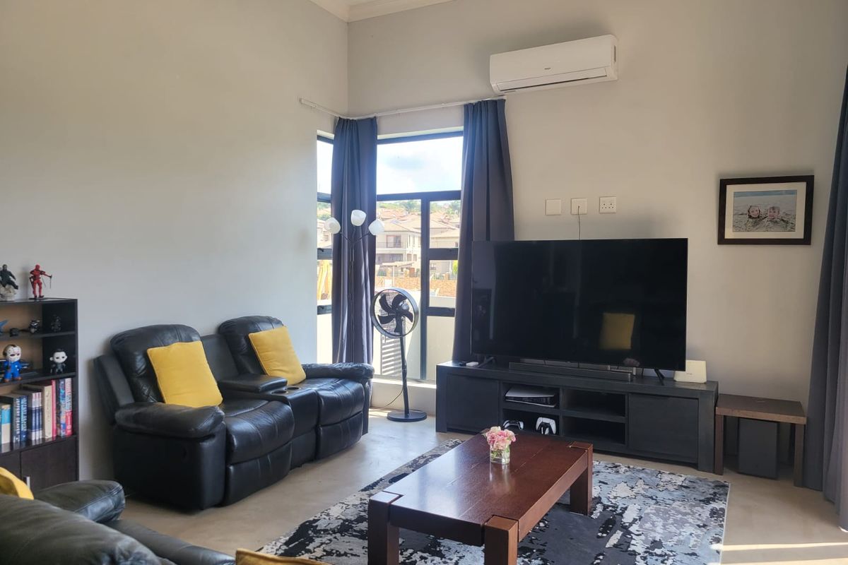 A comfortable living room featuring tiled flooring, a split-system air conditioner, and a large window providing natural light.