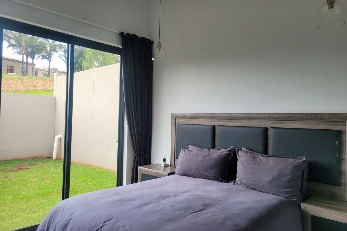 A modern bedroom featuring a built-in headboard, pendant lighting, and large sliding glass doors that provide direct access to the rear garden.