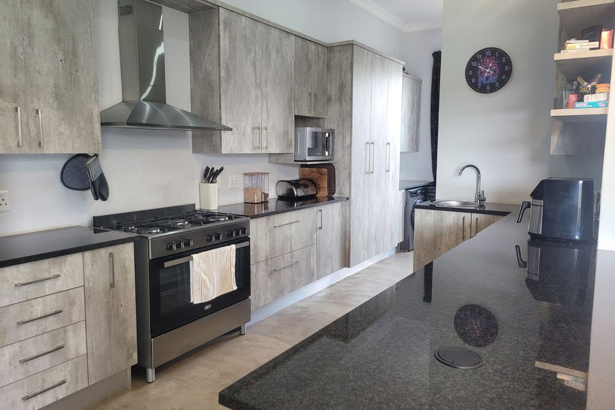Modern kitchen featuring wood-look cabinetry, granite countertops, a gas stove with extractor fan, and a functional island with an integrated sink.