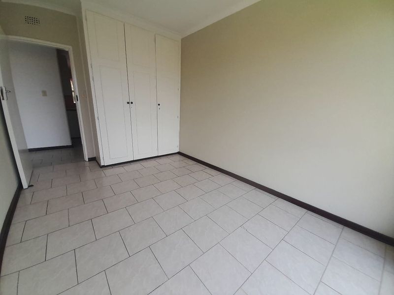 An empty bedroom featuring neutral tiled flooring, built-in cupboards, and simple coving, providing a clean and versatile space.