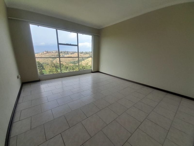 An empty living room featuring large windows with scenic views and neutral tiled flooring, offering a bright and versatile space.
