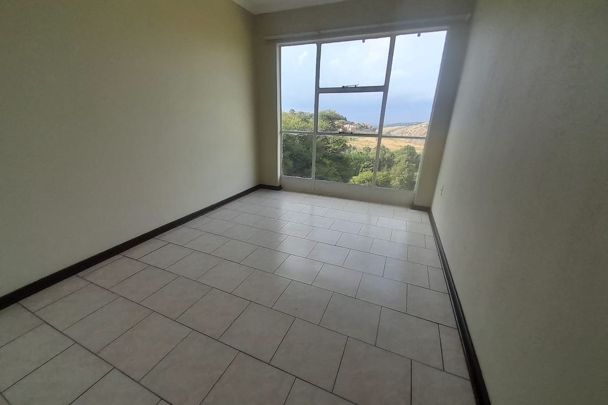 A bright, empty bedroom featuring tiled flooring and a large window with scenic views.