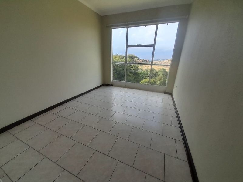 A bright, empty bedroom featuring tiled flooring and a large window with scenic views.