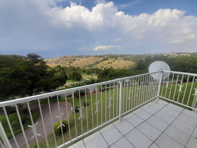 A spacious balcony featuring tiled flooring and a white metal balustrade, offering expansive elevated views over the surrounding landscape and estate grounds.