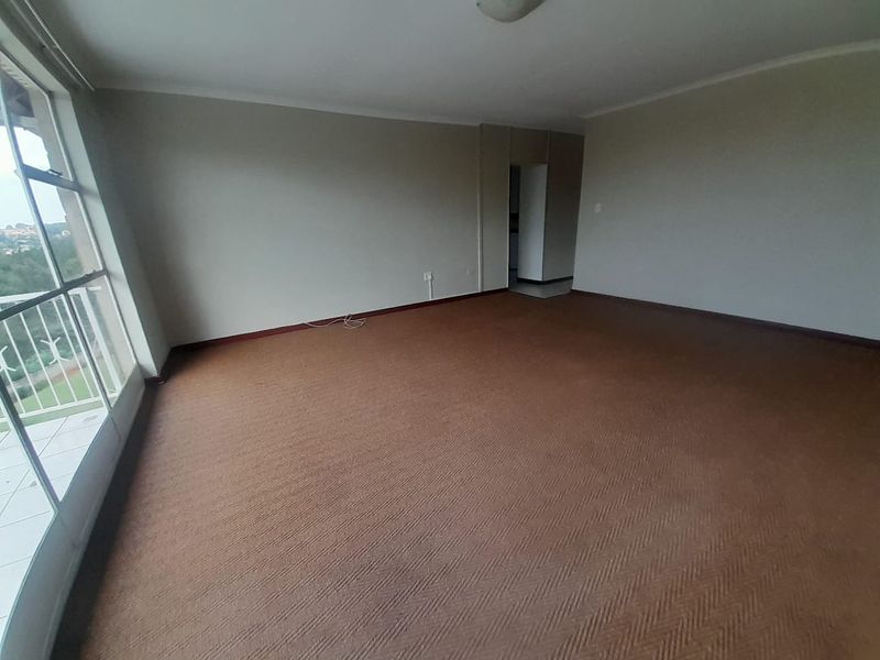 A spacious, empty living room featuring carpet flooring and a large sliding glass door providing access to an outdoor balcony.