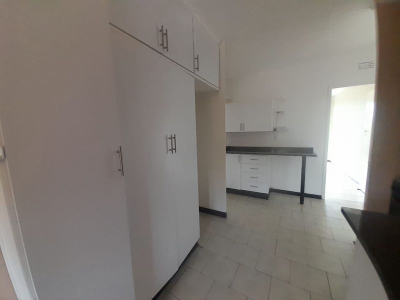 A functional kitchen area featuring white built-in cabinetry, dark laminate countertops, and tiled flooring, offering a clean and neutral space for culinary activities.