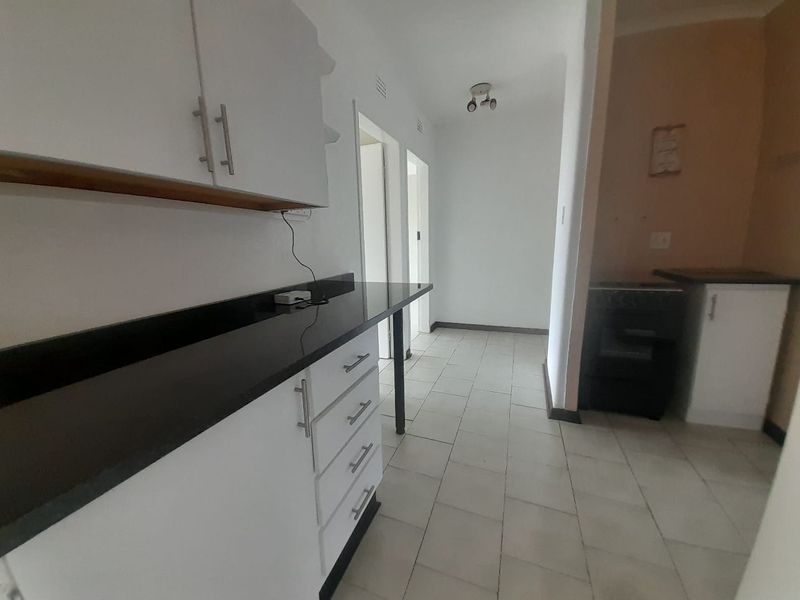 A functional kitchen area featuring white built-in cabinetry, dark stone countertops, and tiled flooring, leading into a hallway.