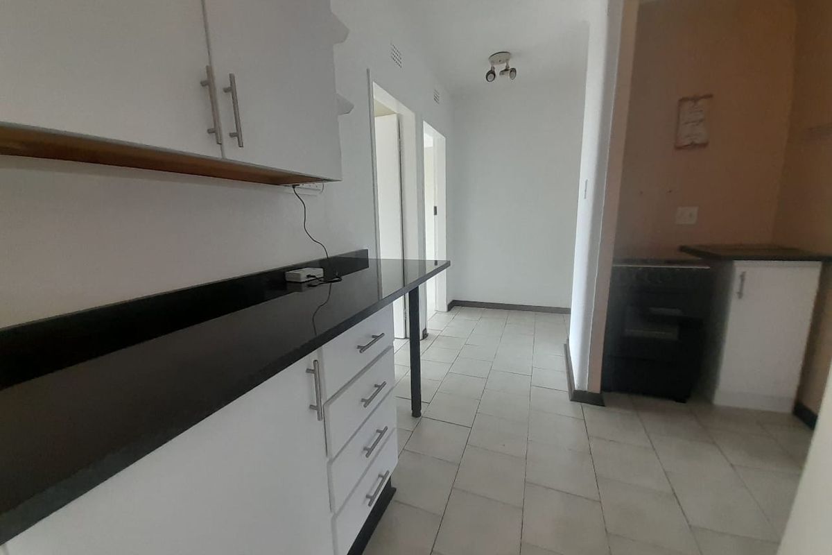 A functional kitchen area featuring white built-in cabinetry, dark stone countertops, and tiled flooring, leading into a hallway.