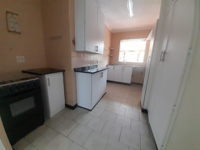 A functional kitchen featuring white built-in cabinetry, tiled flooring, a double sink, and a freestanding stove, offering a practical layout for daily use.