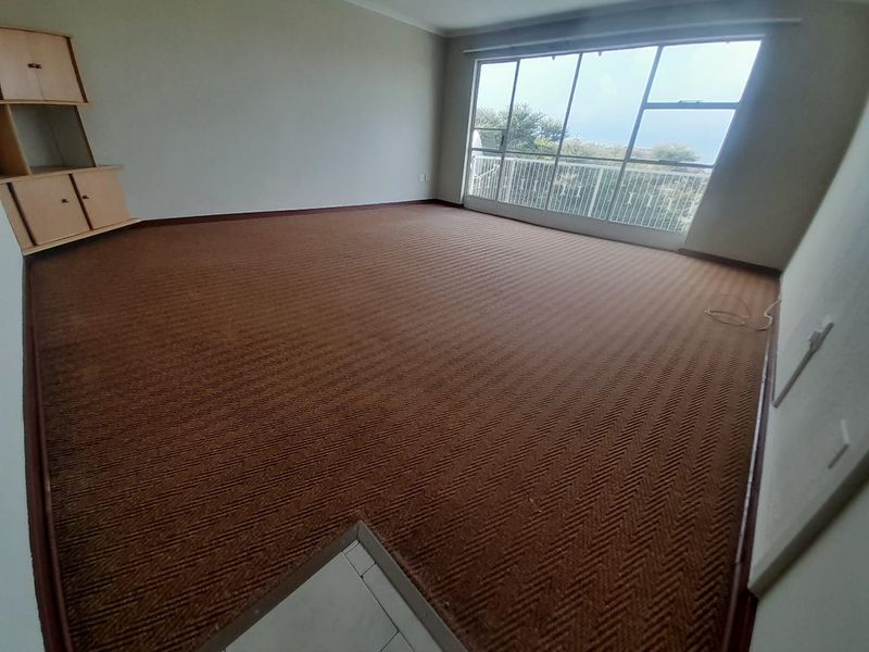 Spacious living area featuring large sliding glass doors leading to a balcony, with neutral walls and carpeted flooring throughout.
